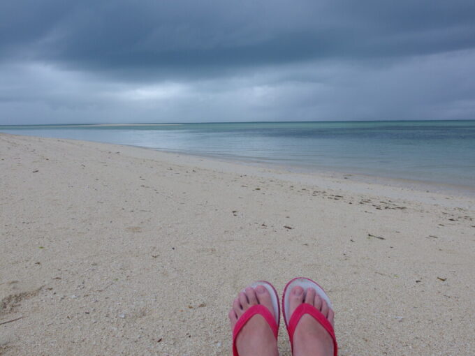 6月中旬梅雨明け間近の竹富島雨上がりの冷たいビーチに座る
