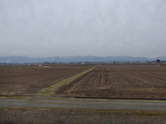 3月中旬春まだ浅い秋田新幹線こまち号車窓から望む枯色の田園と雪景色の山並み