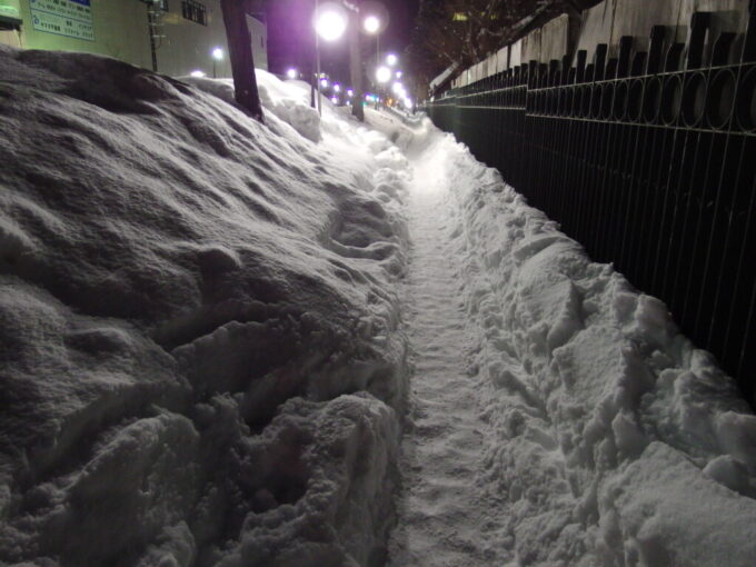 1月中旬冬の北海道大雪の後の札幌うずたかく積もる雪の脇を慎重に歩く