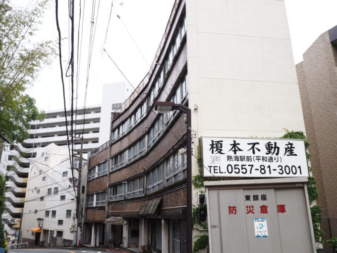 5月末雨上がりの熱海坂道に沿うように建つ近代店舗企画の文字が書かれた渋いビル