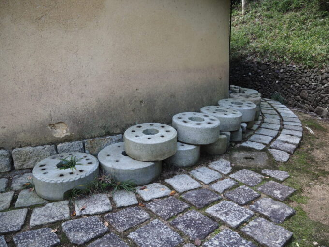 10月下旬初めての屋島四国村ミウゼアム四角い形をした上原家砂糖しめ小屋の周囲に置かれたしめぐるま石臼