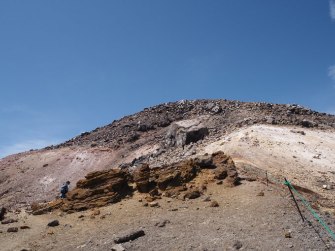 4月中旬春うららの那須岳主峰茶臼岳山頂へと向かう登山道行く手に立ちはだかる茶色い岩とその先に鎮座する大岩