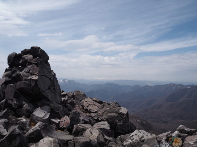 4月中旬春うららの那須岳主峰茶臼岳山頂で白銀の会津の山並みを見ながら岩に腰掛け休憩